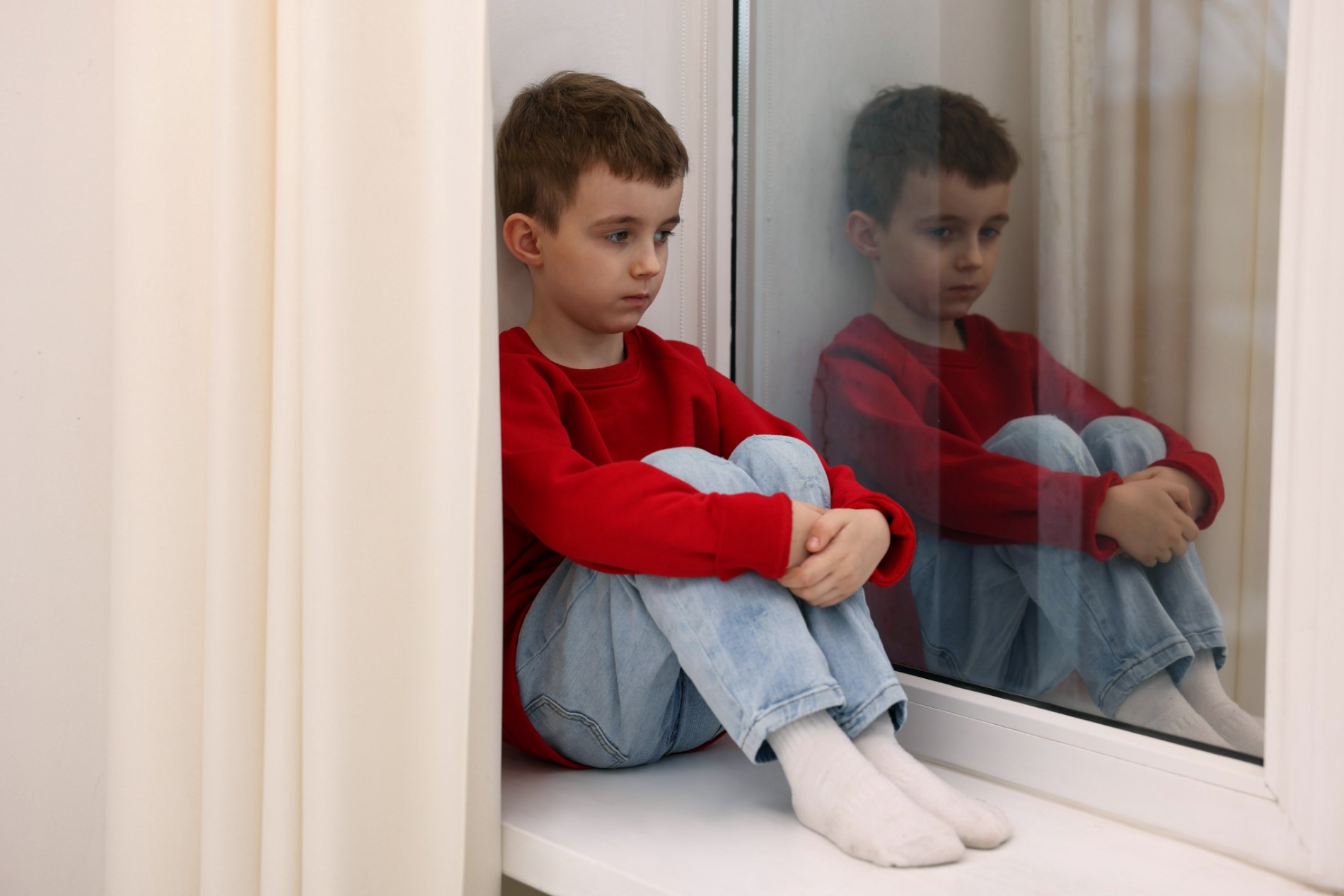 Junge sitzt nachdenklich am Fenster